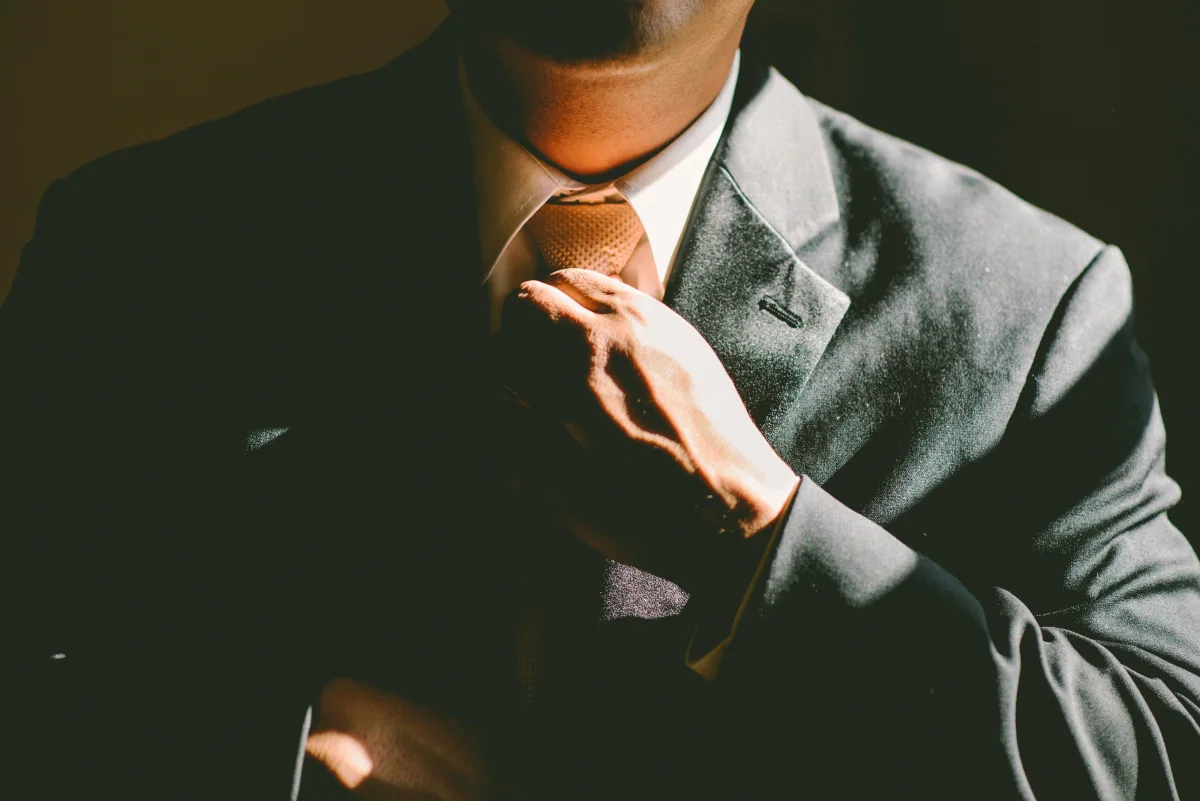 A man in a suit, touching his tie as if to tighten it.